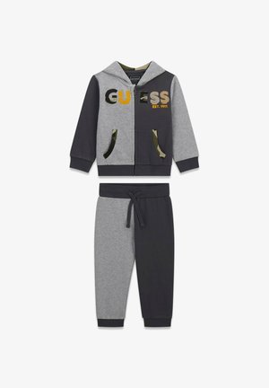 Loungewear-Set bestehend aus einem Zip-Hoodie mit grauen und schwarzen Farbblöcken, „GUESS“-Logo und passenden tapered Pants mit camo-gefütterten Taschen.