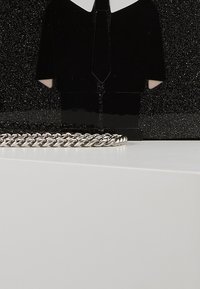 Black figurine in suit with white shirt and tie, plastic material, beside a silver chain laying on a white surface, against a black background.