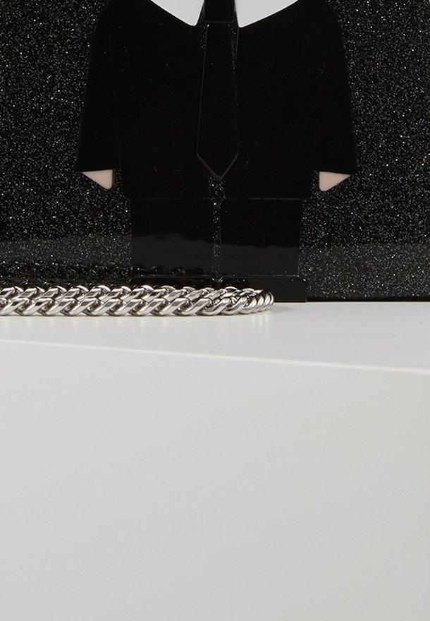 Black figurine in suit with white shirt and tie, plastic material, beside a silver chain laying on a white surface, against a black background.