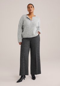 Grau gestrickte Strickjacke mit lockerem Schnitt, V-Ausschnitt und Knopfleiste. Kombiniert mit schwarzen weit geschnittenen Hosen mit strukturiertem Muster.