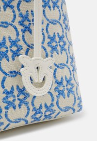 Sac en tissu beige avec des motifs floraux brodés en bleu et une languette de tirage en cuir blanc présentant un design découpé stylisé.