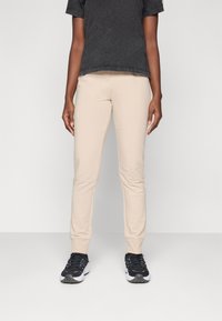 Pantalons de jogging beige fuselés avec une texture lisse, associés à un t-shirt noir à manches courtes et des chaussures de sport noires. Design simple.