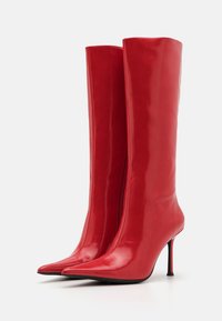 Red, glossy knee-high boots with a pointed toe and high stiletto heel. Features a side zipper for closure and a smooth texture.