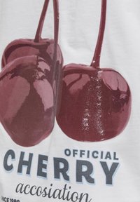 Biała koszulka z dużym graficznym nadrukiem błyszczących czerwonych wiśni oraz napisem "Oficjalne Stowarzyszenie Wiśniowe" w kolorze niebieskim.