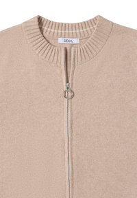 Beige zip-up cardigan i mjukt material, med ribbad hals och silverfärgad dragkedja med rund dragare. Rena, minimalistiska linjer.