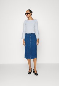 Top lung cu mâneci lungi de un albastru deschis, cu detalii de tip funda, asortat cu o fustă din denim închis până la genunchi. Pantofi cu toc bloc negri și ochelari de soare.