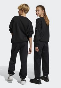 Conjunto de sudadera y pantalones de chándal negros, con un corte relajado, puños acanalados y dobladillos de tobillo elásticos, combinado con zapatillas de contraste.