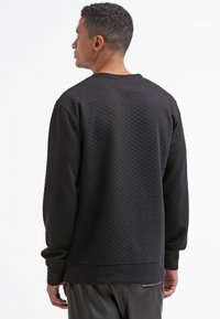Czarny pikowany sweatshirt z długimi rękawami, okrągłym dekoltem i ściągaczami. Miękka tekstura, minimalistyczny design i prosty dół.