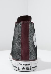 Vysoké tenisky s třpytivým černým plátnem a vínovými semišovými akcenty. Mají gumovou podrážku a ikonické hvězdné logo na boku.