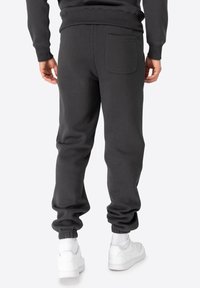 Pantalon de survêtement gris avec des poignets élastiques, doté d'une poche arrière unique. Le matériau a une texture douce, conçu pour le confort et le port décontracté.