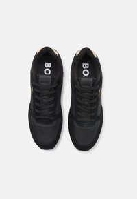 Svart sneakers med en kombinasjon av semsket skinn og mesh-materialer, rund tå, snøring, med logo og gulldetaljer på siden.