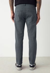 Jeans de denim gris con corte recto, dos bolsillos traseros y una textura sutil. Llevados con zapatillas negras y blancas.