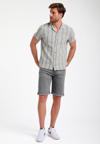 Korte mouwen, lichtgrijze geknoopte blouse met een gestreept patroon, gecombineerd met grijze shorts met omgeslagen zoom en witte sneakers.