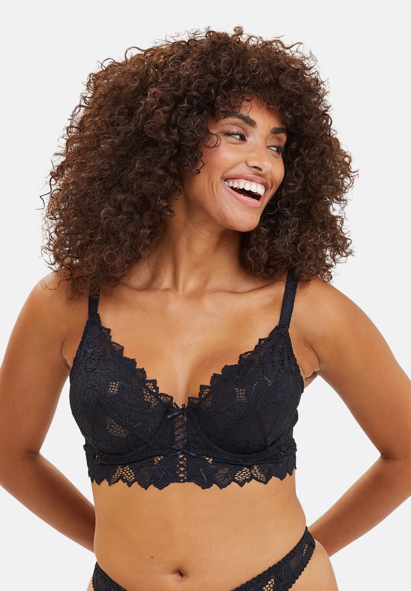 Zwarte kant bralette met geschulpte randen, bloemenpatroon, verstelbare bandjes en een haak-en-oog sluiting aan de voorkant. Glad textuur.