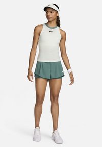 Nike sport tanktop in lichtgroen met bijpassende flared shorts. Kenmerken zijn een hoge hals, mouwloos ontwerp en het kenmerkende Nike-logo.