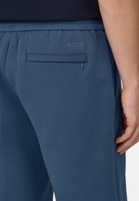 Pantaloni jogger morbidi di colore blu, realizzati in tessuto leggero, con vita elasticizzata, tasche laterali e una tasca posteriore con dettaglio a cerniera.