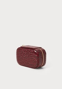 Pequeño estuche rectangular de piel de cocodrilo roja con patrón, con cremallera dorada y cierre de solapa sobre un fondo blanco liso.