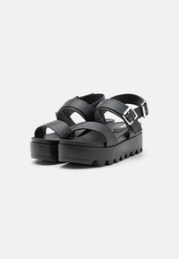 Black platform sandals featuring thick straps, adjustable buckle, and textured rubber sole with a chunky profile.