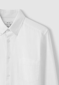 Cămașă albă slim-fit din material neted, cu guler ascuțit, nasturi pe toată lungimea, și un buzunar pe piept pe partea stângă.