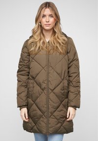 Manteau matelassé en vert olive avec fermeture éclair sur le devant, poches latérales et poignets côtelés. Il possède une capuche et un motif en losanges sur le tissu.