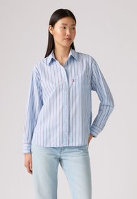 Chemise bleu clair boutonnée avec des rayures rouges verticales, un col pointu, des manches longues et une poche poitrine. Tissu en coton lisse.