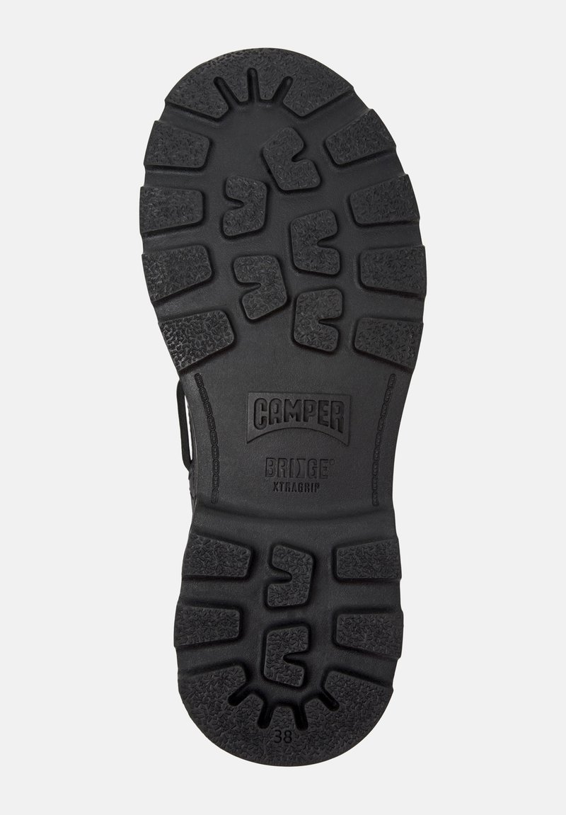 Sort gummisko sål med tekstureret grebmønster og fremtrædende logo med teksten "Camper Bridge XTRAGRIP." Har dybe riller for godt fodfæste.