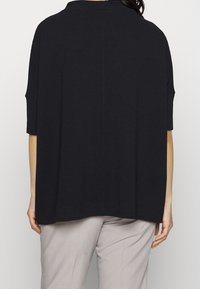 Schwarzes, oversized Oberteil mit kurzen Ärmeln, strukturiertem Stoff und rundem Halsausschnitt. Verfügt über einen geraden Saum und einen lockeren Schnitt für optimalen Komfort.