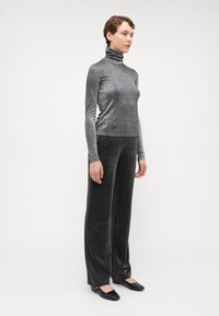 Haut col roulé gris métallique à manches longues, associé à un pantalon noir à sequins larges et à des chaussures plates noires. Fond blanc uni.