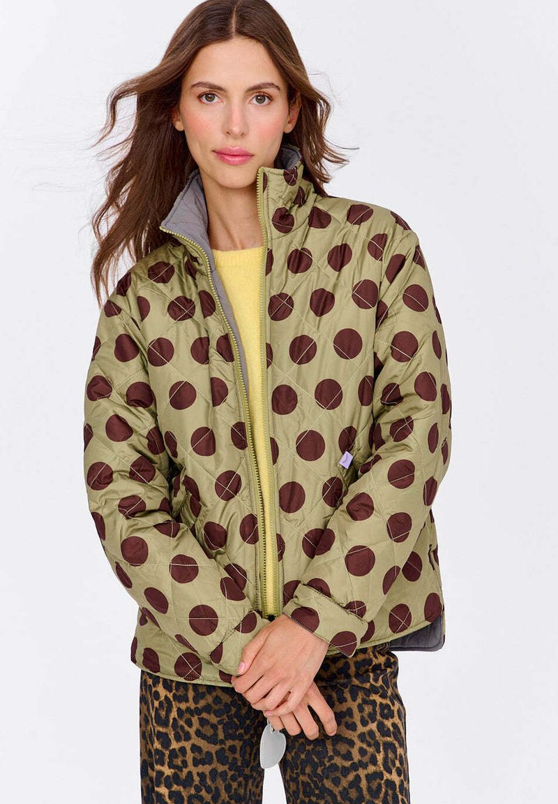 Zelená prešívaná bunda s veľkými hnedými bodkami, sivou podšívkou, vysokým golierom a zipsom. Nosí sa cez žltý top so zvieracím vzorom a nohavicami.