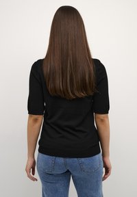 Top corto a maniche corte nero in maglia con scollatura rotonda, abbinato a jeans blu a vita alta. Tessuto liscio con un design aderente.