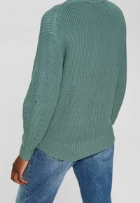 Sweter dziewiarski w stonowanej zieleni, o przewiewnej strukturze z ribbingu przy mankietach i dolnej krawędzi, z delikatnymi detalami po bokach i luźnym krojem.