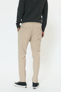Beżowe spodnie o dopasowanym kroju, z tylnymi kieszeniami zapinanymi na guziki, zestawione z czarnymi trampkami i ciemnym swetrem.