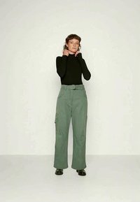 T-shirt de manga longa preta combinado com calças cargo verdes de cintura alta, com bolsos laterais e um cinto. Tecido liso e texturizado. Sapatos pretos.