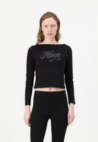 Svart langermet cropped topp med et krystalldekorert "Hug"-logo over brystet, laget av et mykt og stretchy stoff.