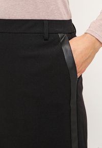 Pantalones negros con un diseño elegante, que presentan una franja lateral lisa y bolsillos. La tela parece suave con un acabado texturizado.