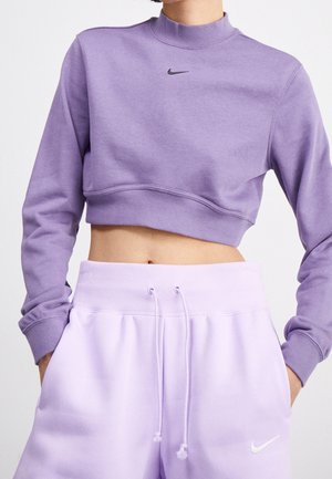 Persoon draagt een cropped lavendelkleurige Nike-trui en bijpassende lavendelkleurige joggingbroek met zichtbare zakken met trekkoorden.