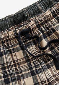 Tan and dark blue plaid shorts with an elastic waistband, drawstring detail, and textured fabric featuring various checked patterns.