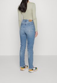 Modré denimové džíny s vysokým pasem a třepenými lemy. Nosené s dlouhým rukávem olivového topu a barevnými teniskami s kombinovanými materiály a akcenty.