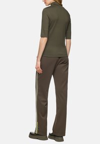 Olive green short-sleeve top paired with brown textured pants featuring side stripes in yellow and white. Includes a high collar and relaxed fit.