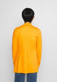 Blazer manica lunga in tessuto arancione brillante, con vestibilità sartoriale, spacco posteriore e design minimalista con un dettaglio logo sottile al collo.