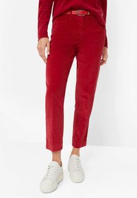 Rote Corduroyhosen mit glatter Textur, schmalem Bein-Design und passendem Gürtel. Kombiniert mit weißen Sneakers für einen lässigen Look.