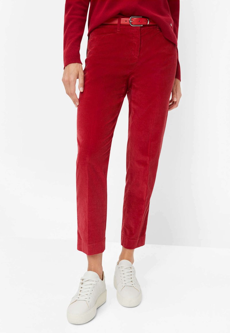 Rote Corduroyhosen mit glatter Textur, schmalem Bein-Design und passendem Gürtel. Kombiniert mit weißen Sneakers für einen lässigen Look.