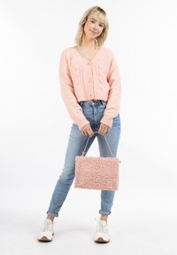 Cardigan cropped rosa e morbido con design a trecce e tre bottoni, abbinato a jeans azzurri e una borsa rosa con texture.