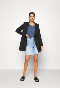 Stripet svart blazer, blå t-skjorte, lyseblå denimskjørt med frynser, og svarte sandaler med åpen hæl. Liten svart håndveske som tilbehør.