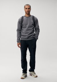 Gray sweatshirt with a round neck and logo, paired with black cargo pants featuring pockets. Light shoes with a multi-color sole.