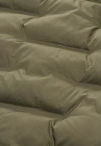 Krupni plan maslinasto-zelenog kviltanog materijala s mekanim, podstavljenim dijelovima i vidljivim šavovima.