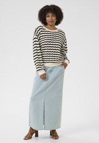 Pull en tricot rayé noir et blanc, avec une coupe ample, associé à une jupe maxi en denim bleu clair avec une fente à l'avant et des sandales à talons marron.
