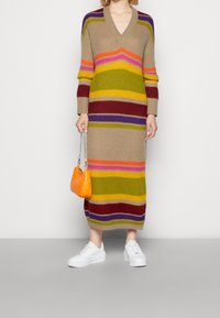 Stickad klänning med V-ringning, prydd med djärva horisontella ränder i beige, gult, grönt, lila, rött och orange. Accessoarer inkluderar en orange väska.