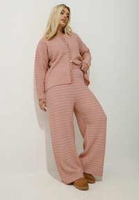Ljust rosa stickad lounge-set med en knapp-up cardigan och vida byxor, båda med ett texturerat mönster. Mjuk tyg med avslappnad passform.