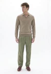 Beige langslévige poloshirt met een kraag, gecombineerd met losse olijfgroene broeken en bruine veterschoenen. Zachte textuur en casual pasvorm.